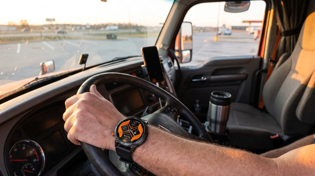 Truck driver's hand on the steering wheel at dawn wearing a Horonix Pathfinder Ultra, phone in a dash mount, highway ahead